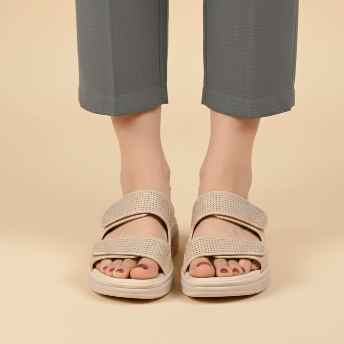 Person wearing beige sandals and gray pants on a beige background