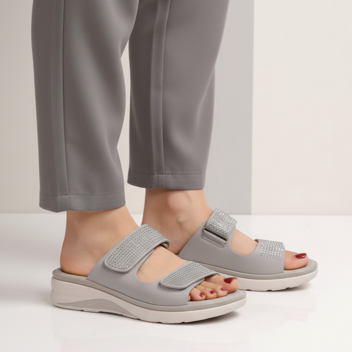Gray sandals worn with gray pants on a neutral background