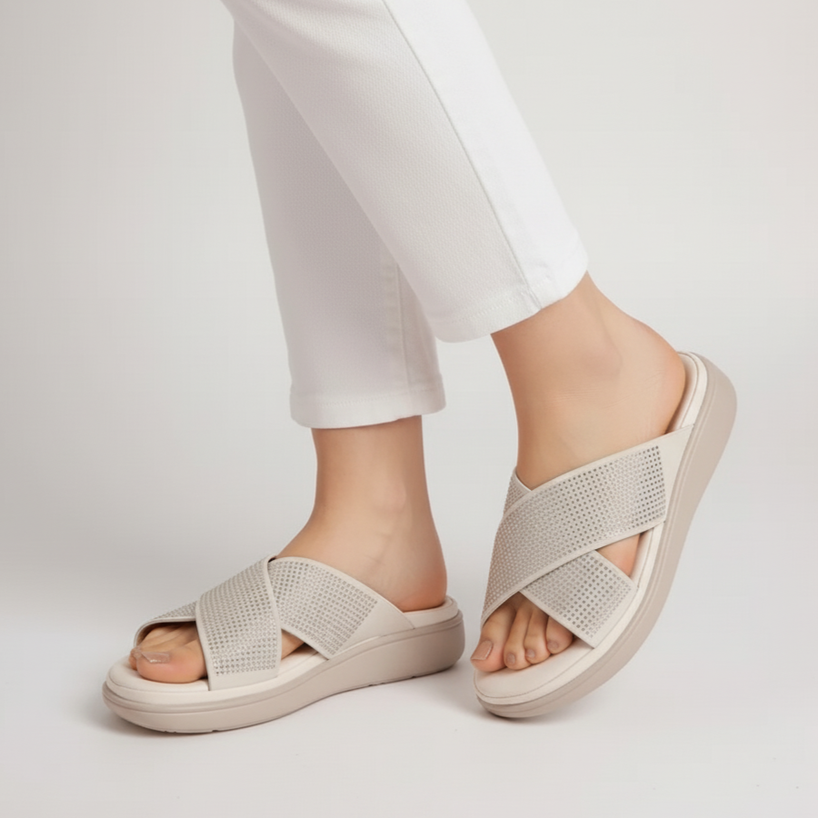 Beige sandals worn with white pants on a light gray background
