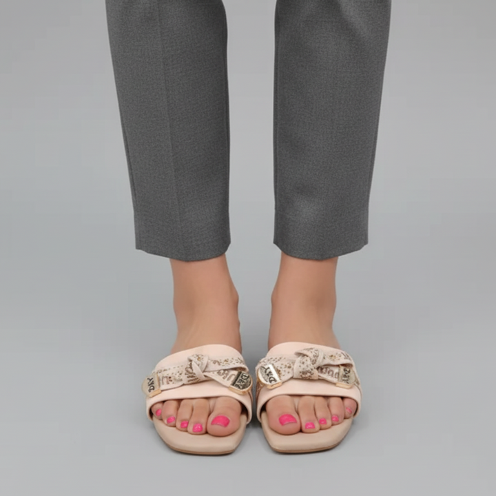 Beige sandals with decorative straps worn with gray pants on a gray background