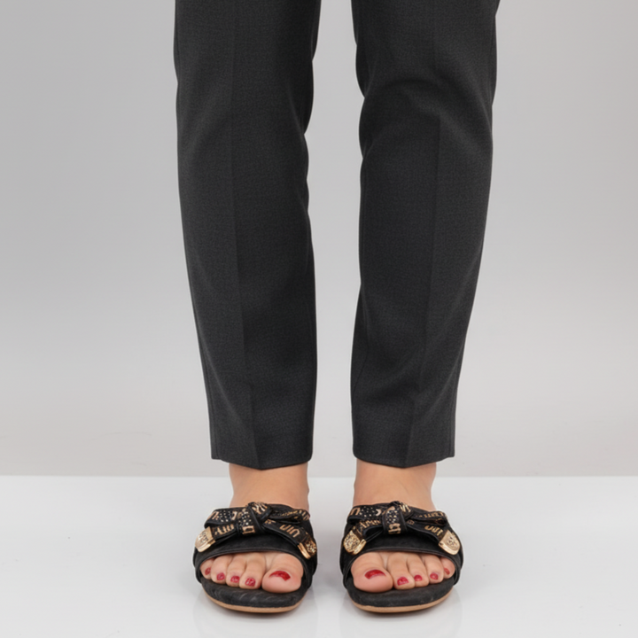 Person wearing black sandals with gold accents and black pants on a light gray background