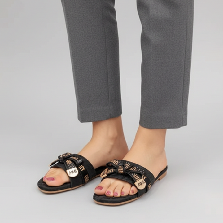 Black sandals with gold accents worn with gray pants on a light gray background