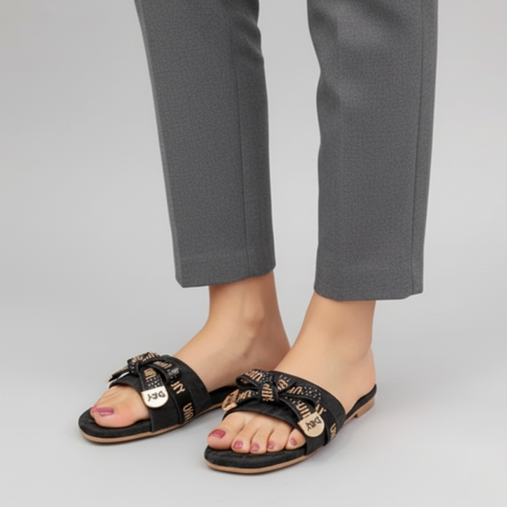Black sandals with gold accents worn with gray pants on a light gray background