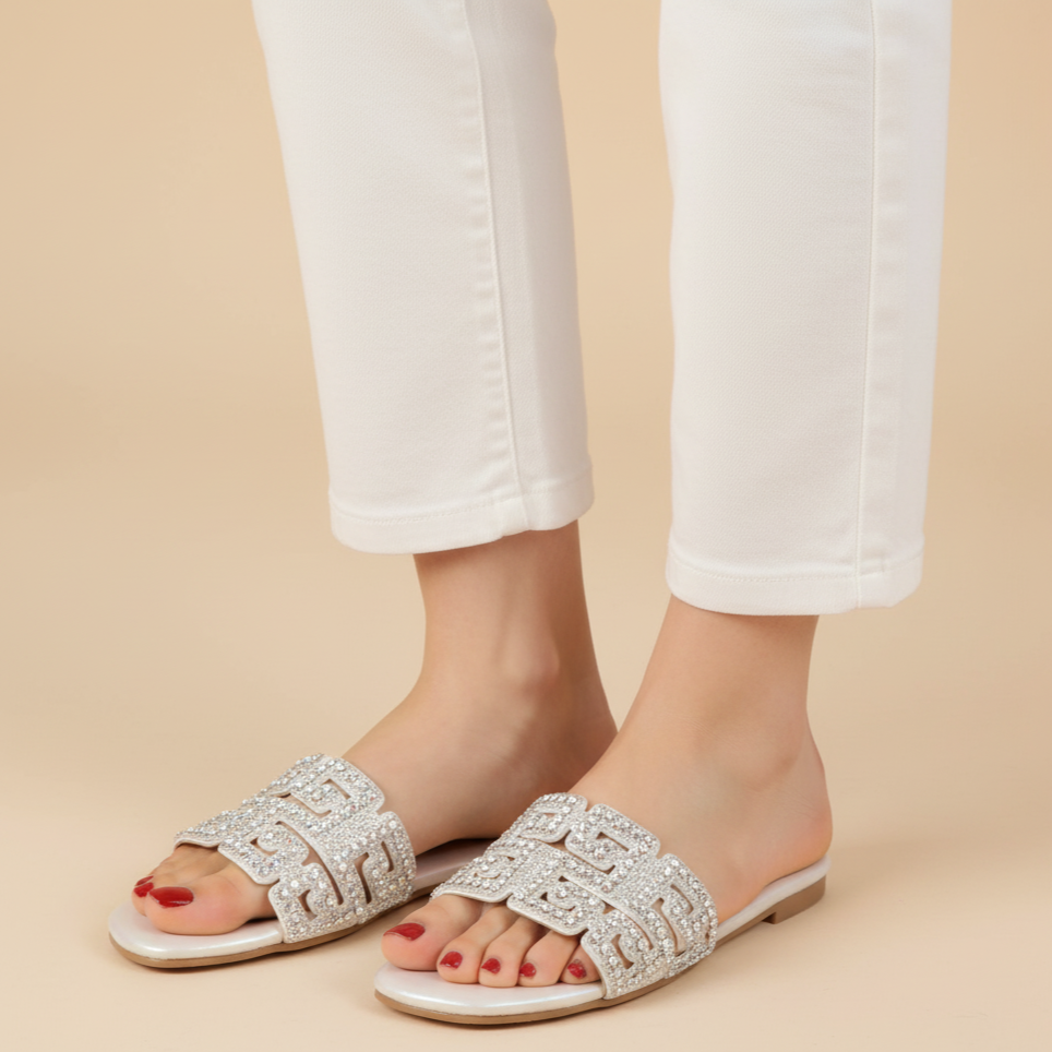 Silver embellished sandals worn with white pants on a beige background
