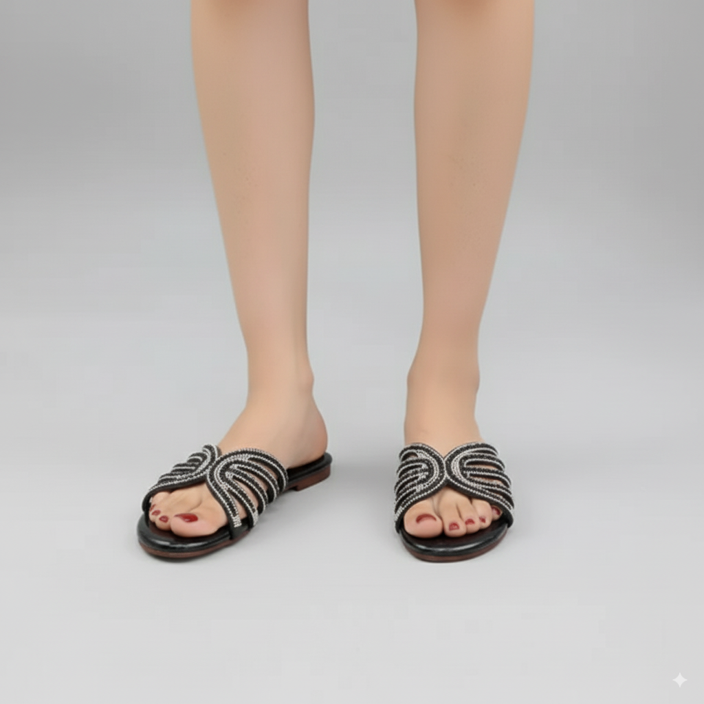 Black sandals with decorative straps worn by a person on a gray background