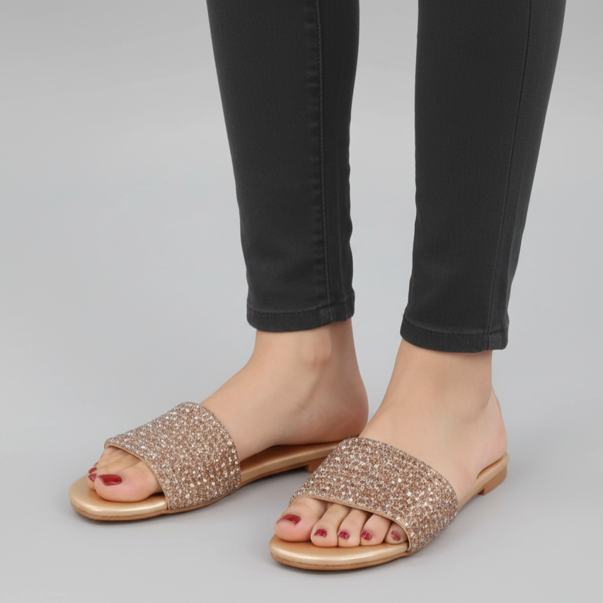 Gold embellished sandals worn with black pants on a gray background