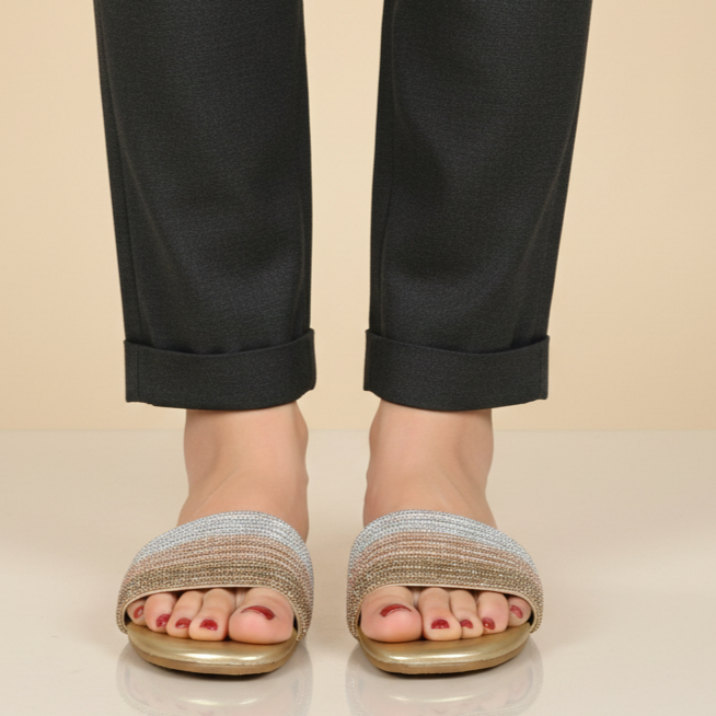 Person wearing black pants and gold sandals on a beige background