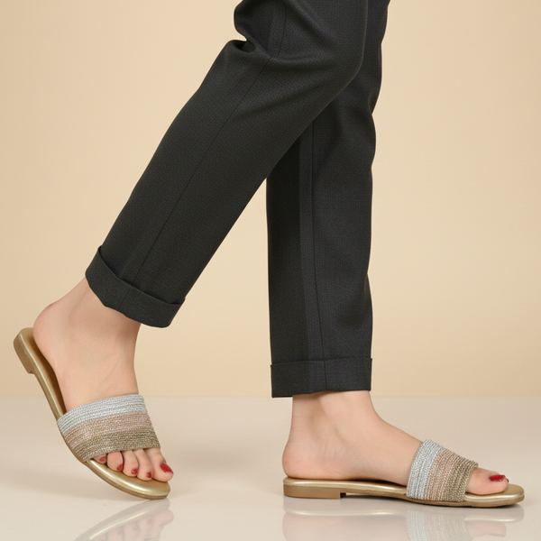 Person wearing gold sandals with striped straps on a beige background