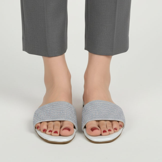 Person wearing gray slides with white soles on a plain background