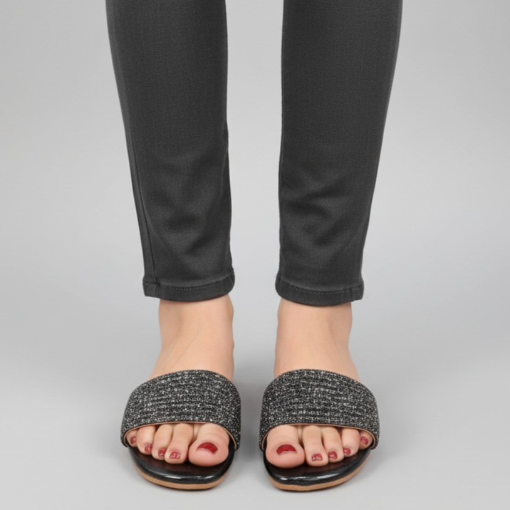 Person wearing black pants and black sandals on a gray background