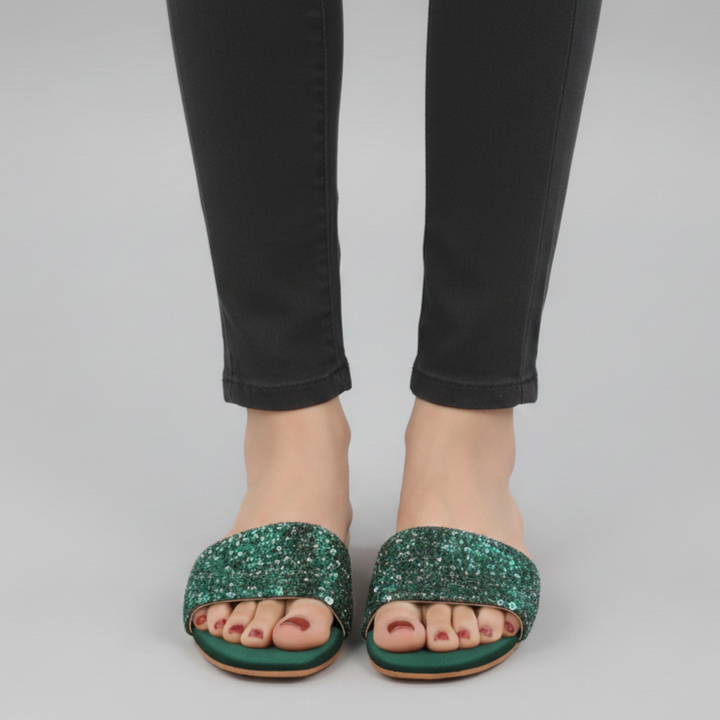 Green glittery sandals worn with black pants on a gray background