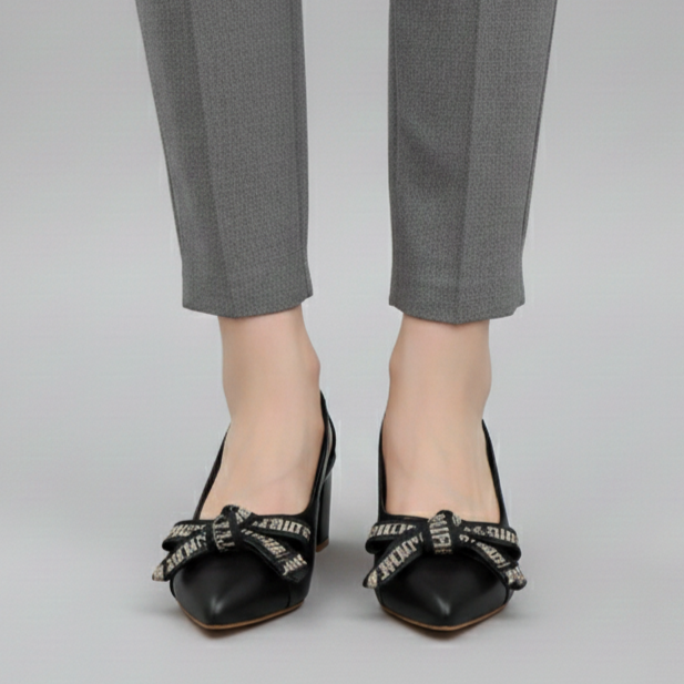 Person wearing gray pants and black shoes with decorative bows on a plain background