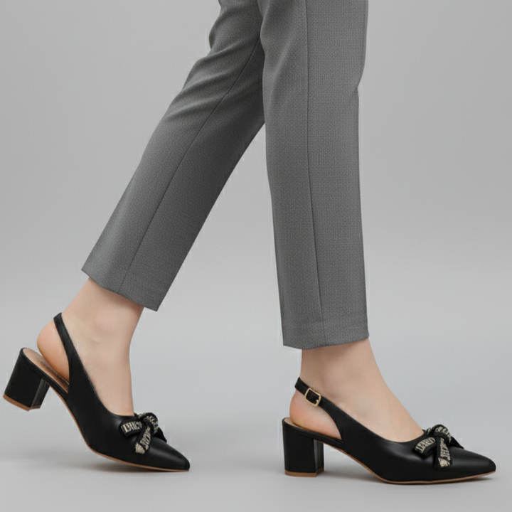 Black shoes with a bow detail worn with gray pants on a light gray background