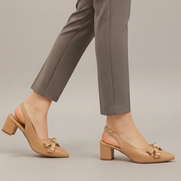 Beige high-heeled shoes with bow details worn with gray pants on a neutral background