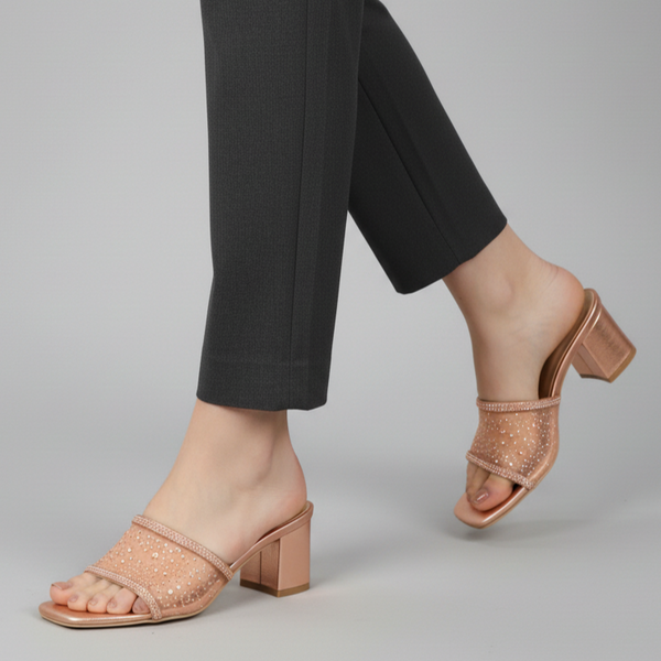 Person wearing rose gold open-toe shoes with a block heel on a gray background