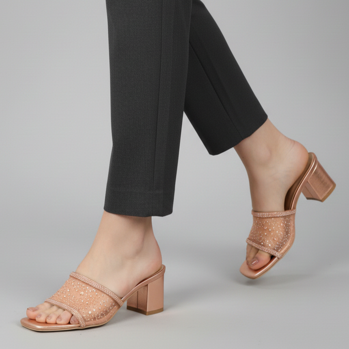 Person wearing rose gold open-toe shoes with a block heel on a gray background