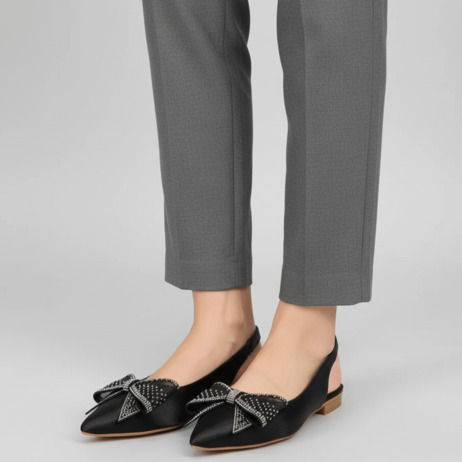 Black shoes with decorative bows worn with gray pants on a light gray background