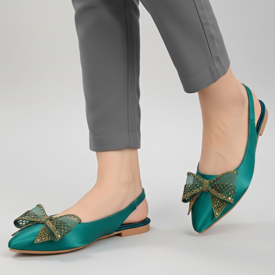 Teal flats with decorative bows worn by a person on a light gray background