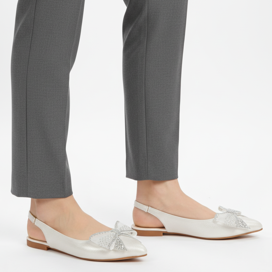 White bow flats worn with gray pants on a white background