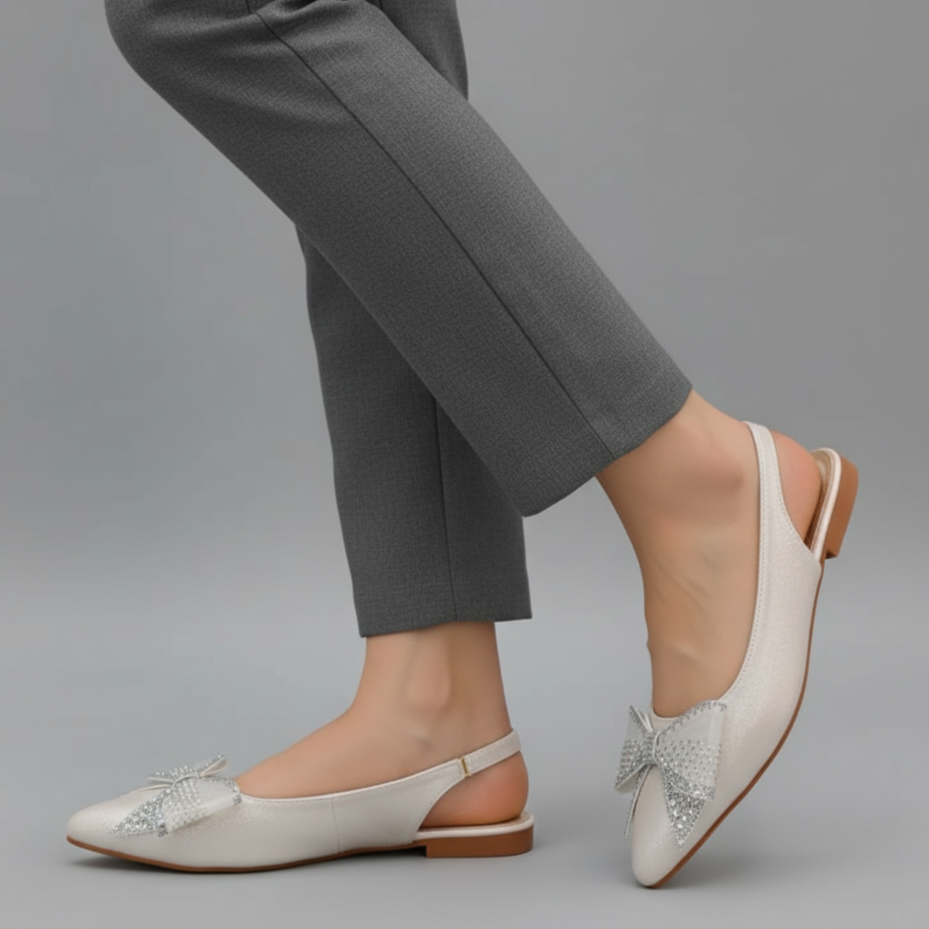 White flat shoes with decorative elements worn with gray pants on a gray background