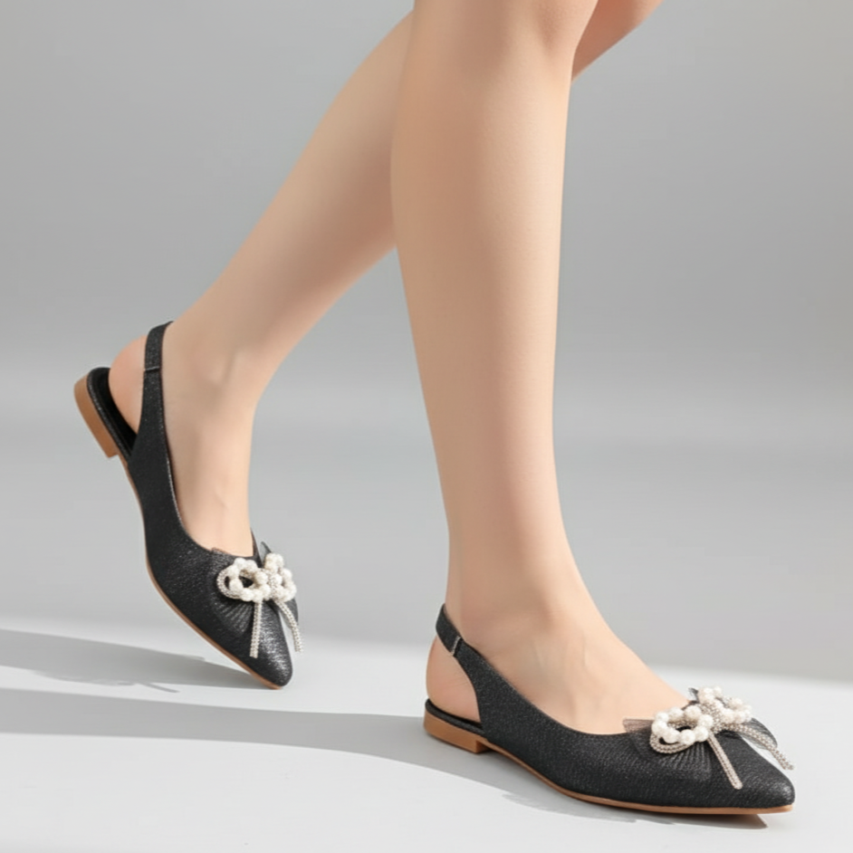 Black flat shoes with decorative bows worn by a person on a gray background