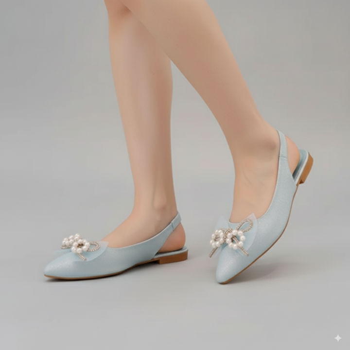 Light blue flat shoes with pearl embellishments worn by a person on a gray background