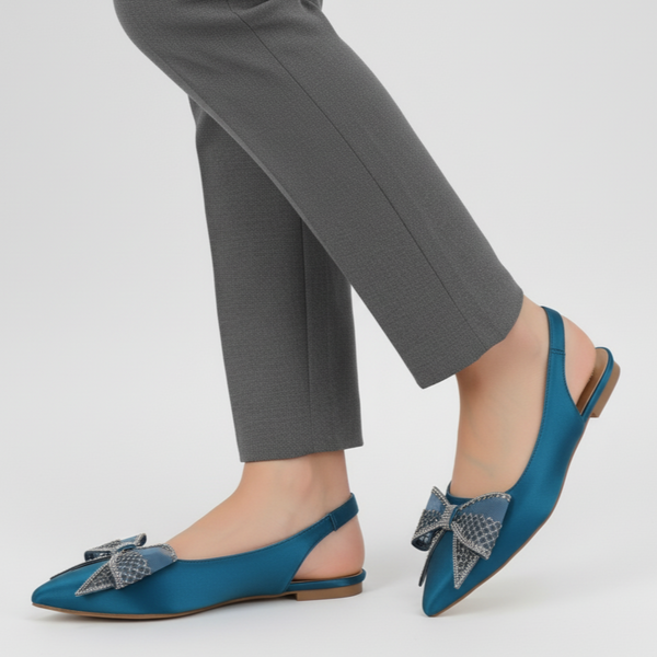Blue flat shoes with decorative bows worn with gray pants on a white background