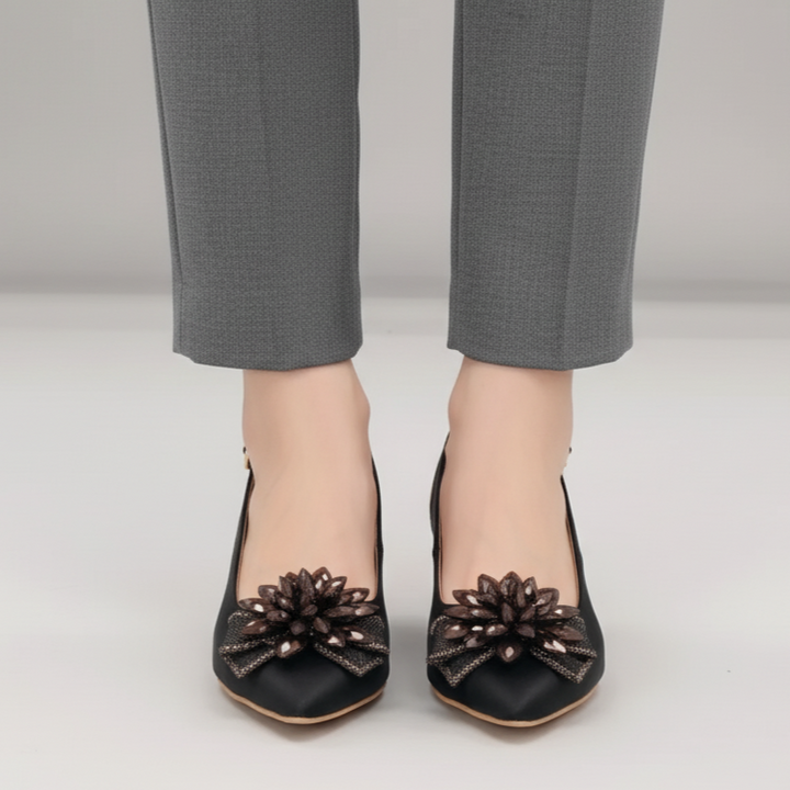 Black shoes with floral designs worn with gray pants on a light gray background