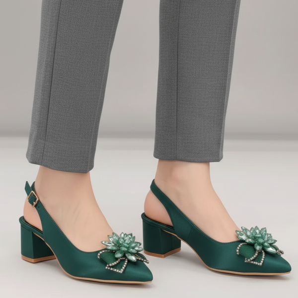 Green high-heeled shoes with floral embellishments worn with gray pants on a neutral background
