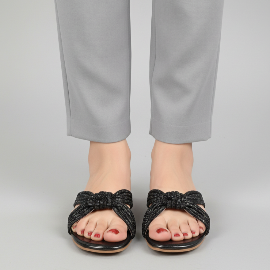 Black bow sandals worn with gray pants on a light gray background