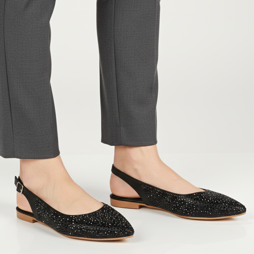 Black embellished flats worn with gray pants on a white background