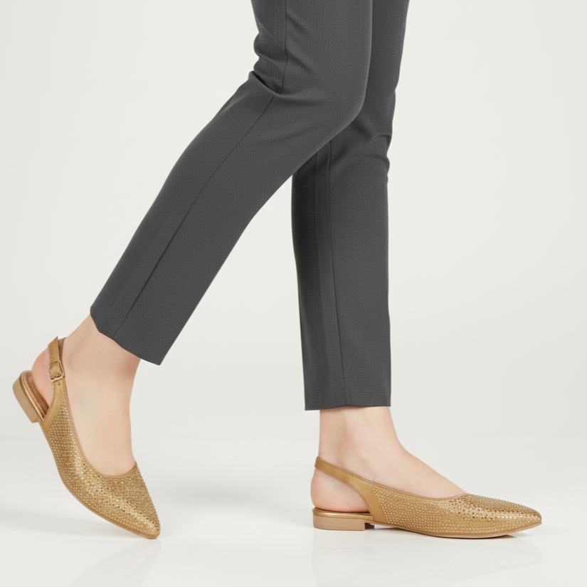 Person wearing gold flats and gray pants on a white background