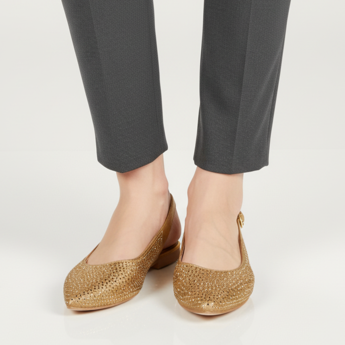 Gold flats worn with gray pants on a white background