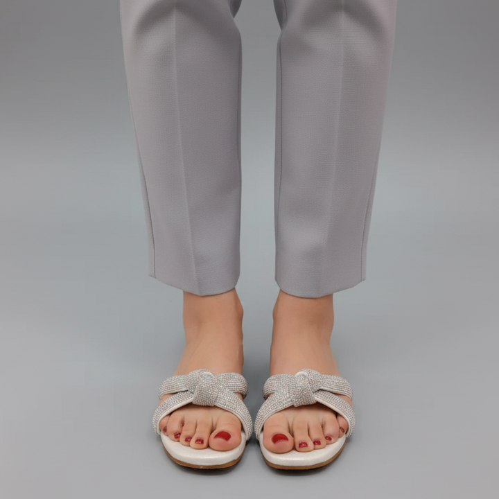 White sandals with bow details worn with gray pants on a gray background
