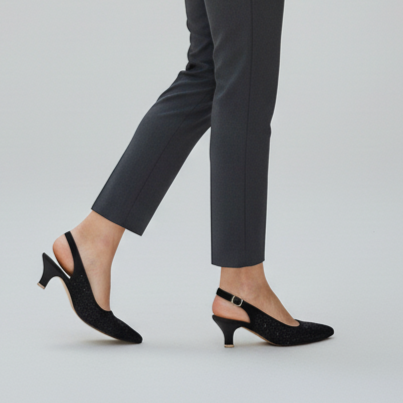 Woman wearing a white shirt and gray pants with a black handbag on a light gray background