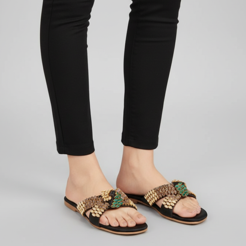 Person wearing black pants and embellished sandals on a gray background