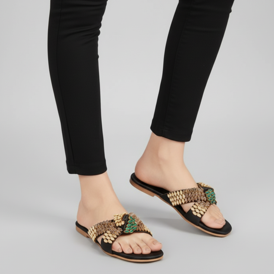 Black sandals with gold embellishments worn with black pants on a gray background