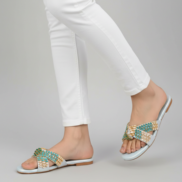 White sandals with gold and turquoise embellishments worn with white pants on a gray background