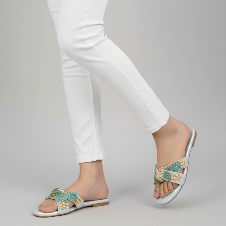 White sandals with decorative straps worn by a person on a gray background