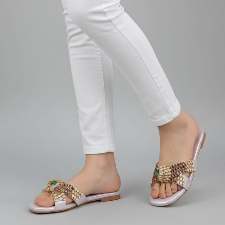 Gold sandals worn with white pants on a gray background
