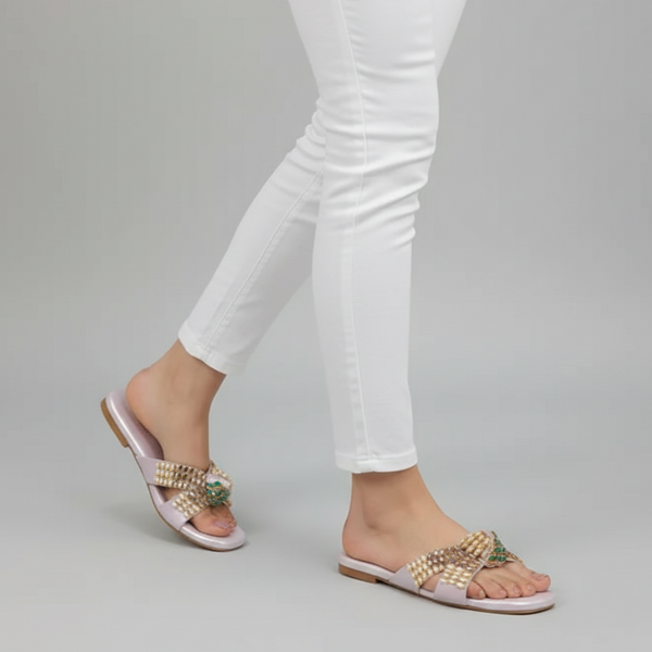 Gold sandals worn with white pants on a gray background