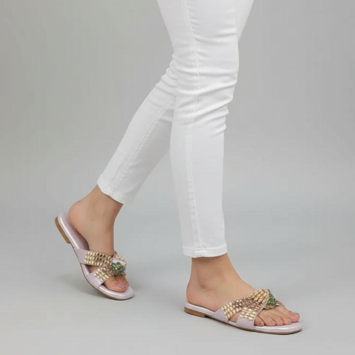 Gold sandals worn with white pants on a gray background
