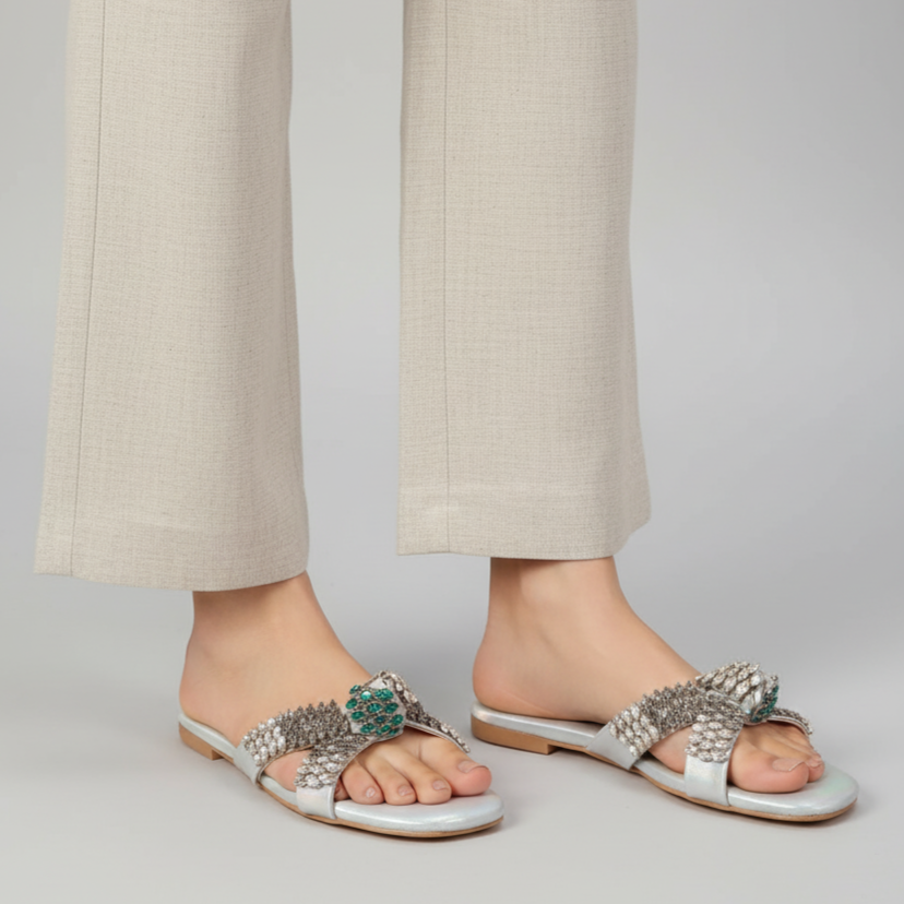 Silver embellished sandals worn with beige pants on a plain background