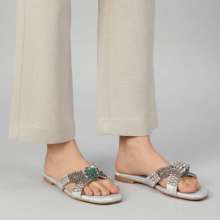 Silver embellished sandals worn with beige pants on a plain background