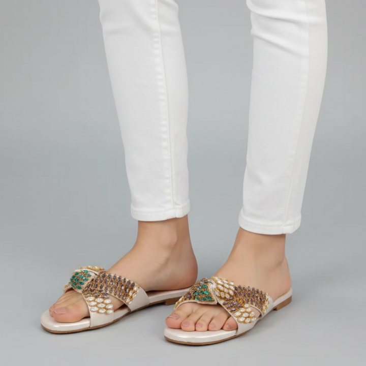 Bejeweled sandals worn with white pants on a gray background