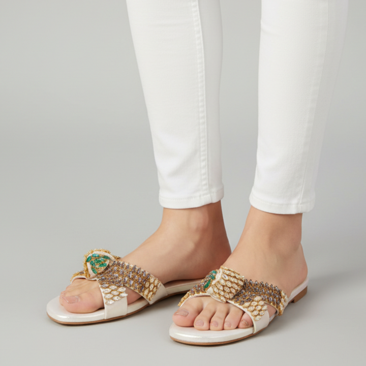 Gold embellished sandals worn with white pants on a gray background