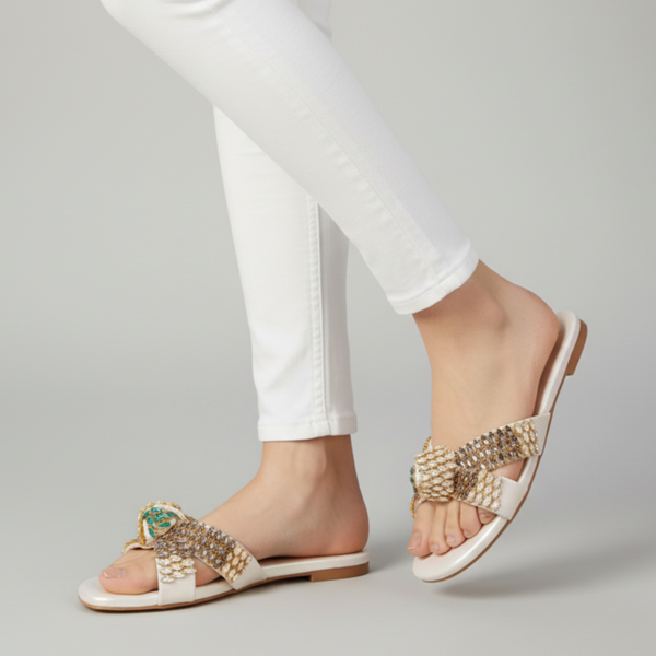 Gold sandals worn with white pants on a gray background