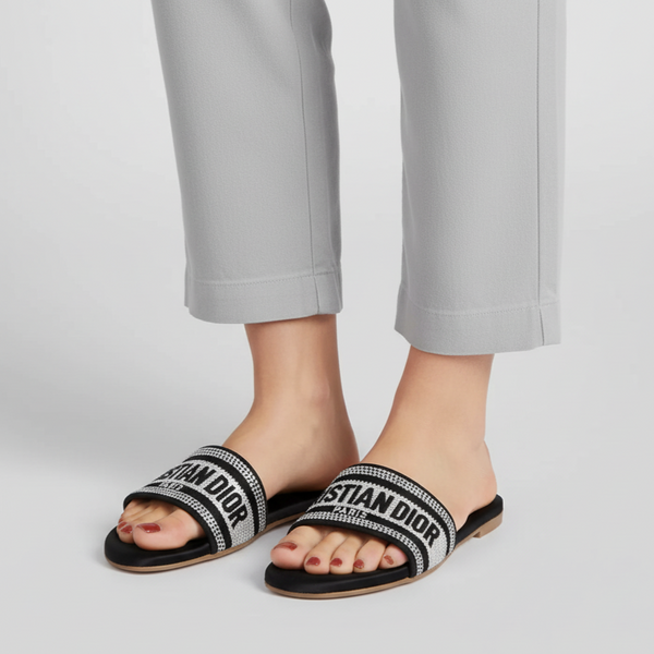 Black slides with 'Christian Dior' branding worn by a person in gray pants on a light gray background