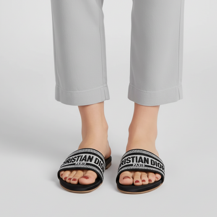 Person wearing black slides with 'Christian Dior' branding on a light gray background