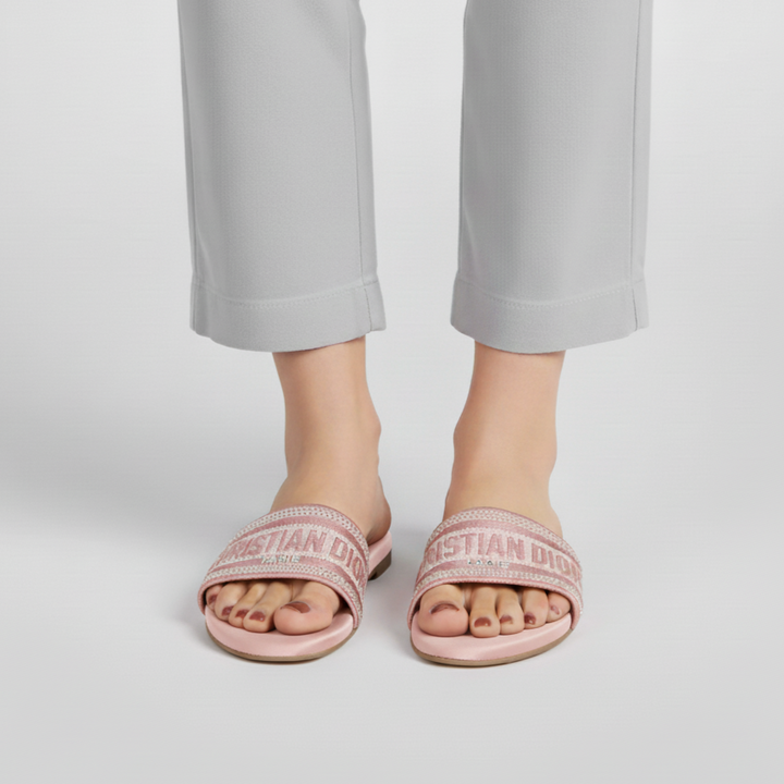 Person wearing pink slides with 'Christian Dior' branding on a white background